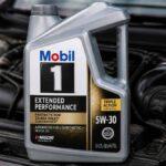 Kanister oleju silnikowego Mobil 1 5W-30 ustawiony przed otwartym silnikiem samochodu