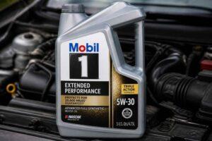 Kanister oleju silnikowego Mobil 1 5W-30 ustawiony przed otwartym silnikiem samochodu