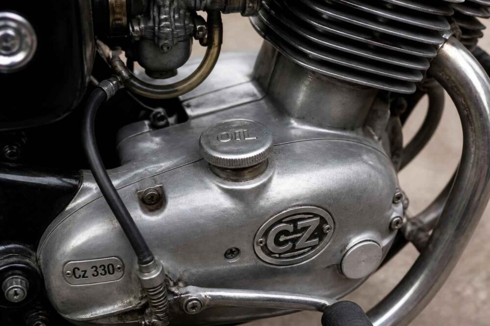 Srebrny silnik motocykla CZ 330 z emblematem CZ Zbliżenie srebrnego silnika CZ 330 z korkiem oleju, emblematem i chromowanym kolektorem wydechowym