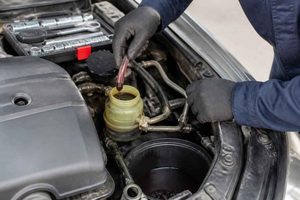 Mechanik uzupełnia płyn wspomagania kierownicy w komorze silnika samochodu